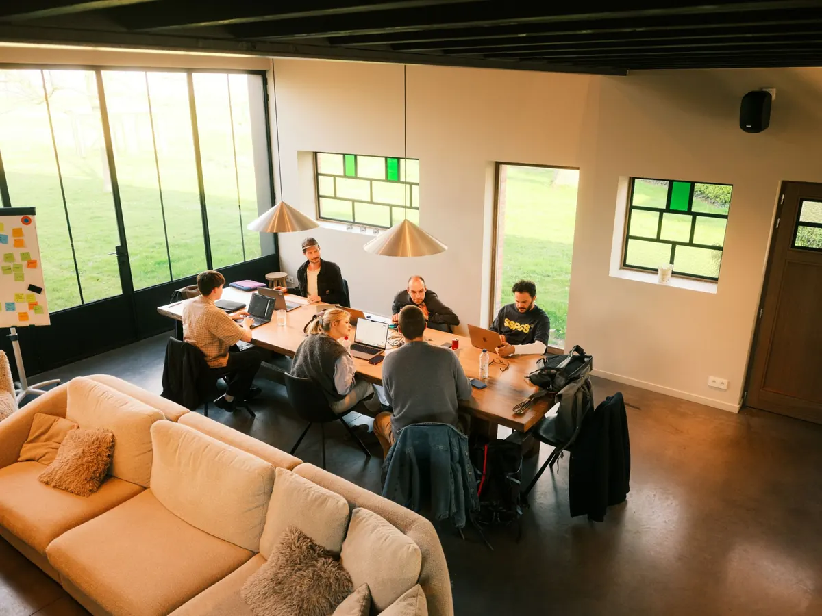 Zes collega’s van Maneuver werken samen aan een lange houten tafel, gezien van boven.