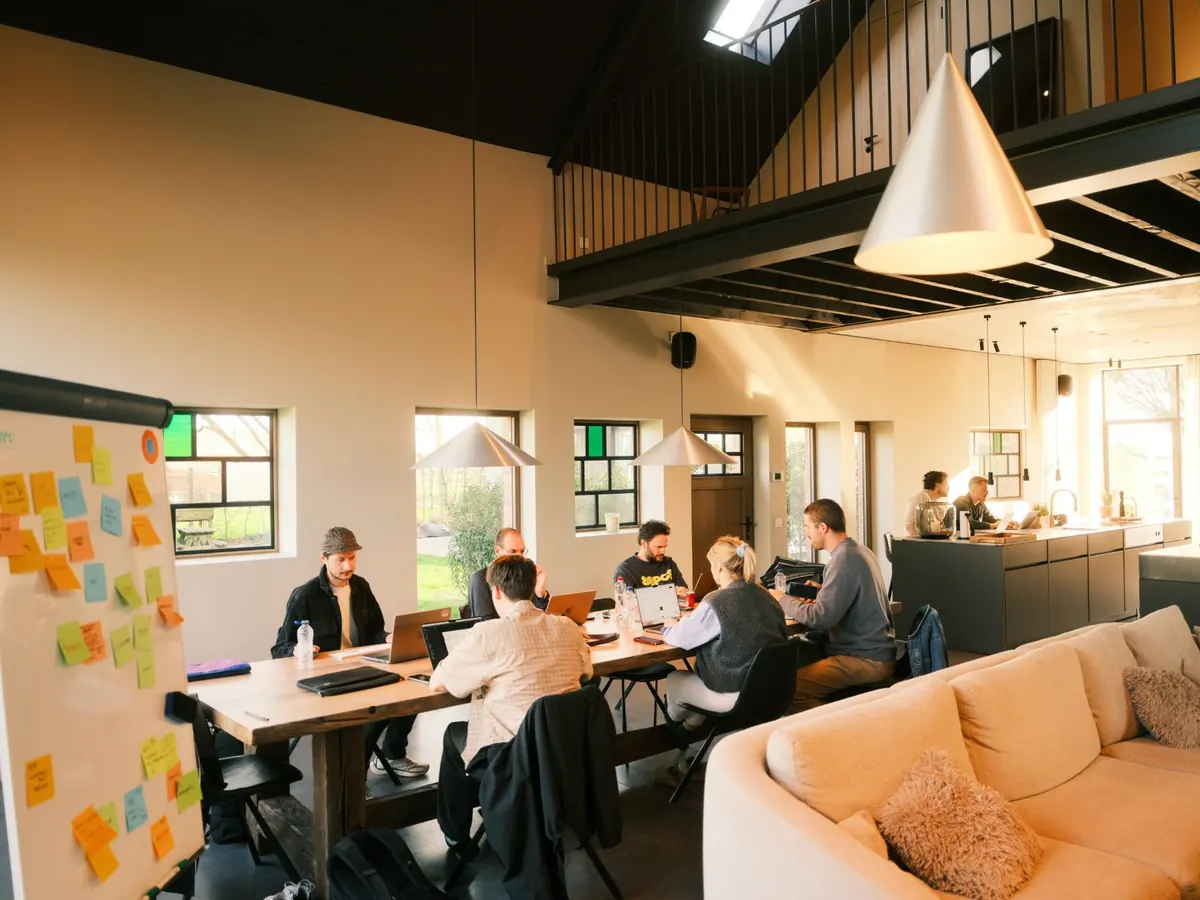 Het team van Maneuver aan een lange houten tafel in een ruime, lichte werkplek met open keuken en zithoek.